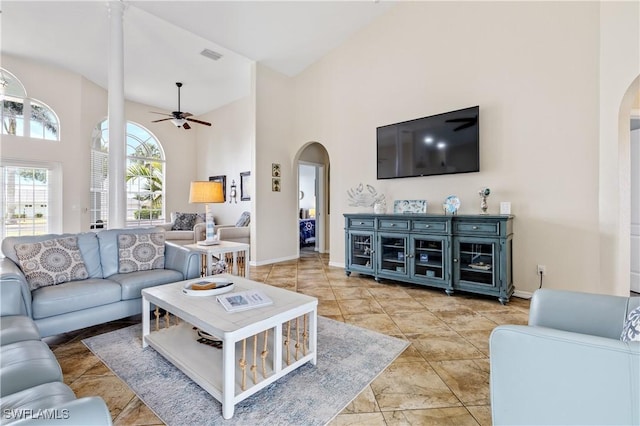 living room featuring visible vents, a ceiling fan, baseboards, a high ceiling, and arched walkways