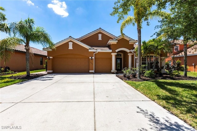 mediterranean / spanish house featuring a tiled roof, a front yard, a garage, concrete driveway, and stucco siding