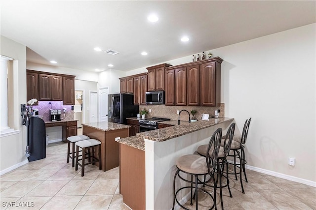 kitchen with visible vents, a kitchen island, a breakfast bar, light stone countertops, and appliances with stainless steel finishes