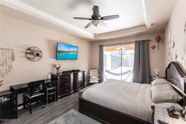 bedroom featuring access to outside, a ceiling fan, wood finished floors, a tray ceiling, and visible vents