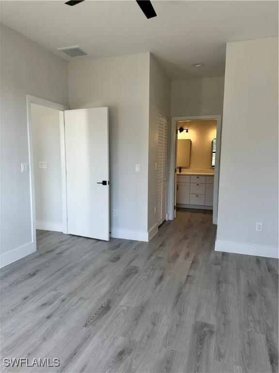 unfurnished bedroom with connected bathroom, baseboards, and light wood-style floors