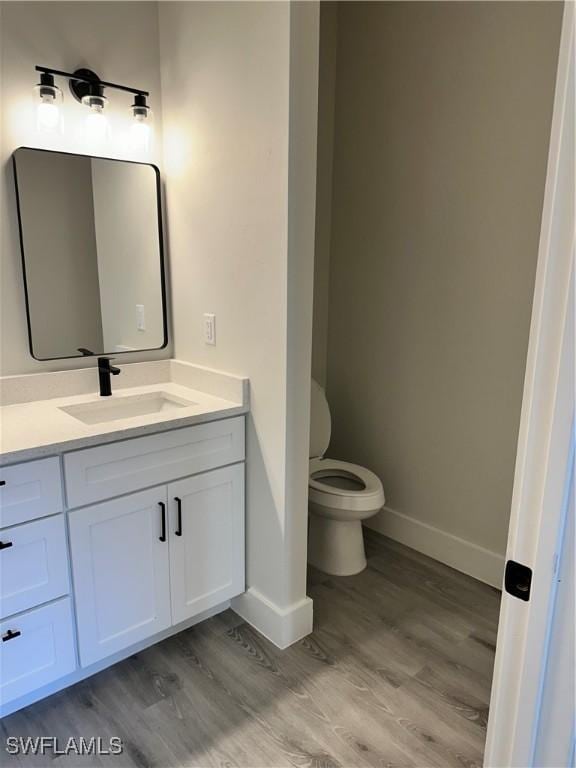 bathroom featuring baseboards, vanity, toilet, and wood finished floors