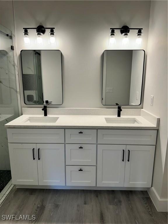 full bath featuring a sink, a marble finish shower, double vanity, and wood finished floors