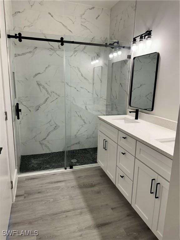 full bathroom with double vanity, a marble finish shower, a sink, and wood finished floors