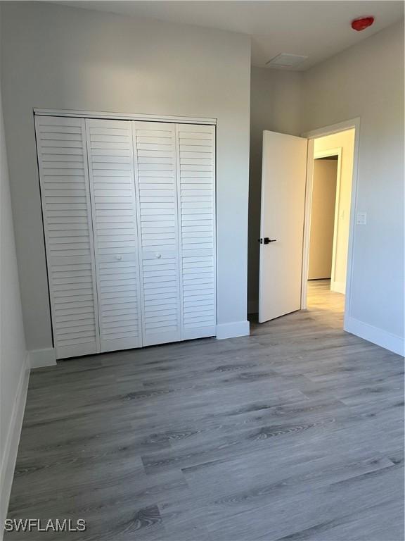 unfurnished bedroom featuring baseboards, wood finished floors, and a closet