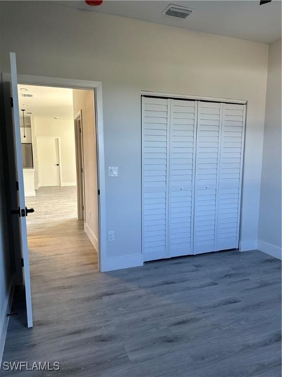 unfurnished bedroom with baseboards, visible vents, wood finished floors, and a closet