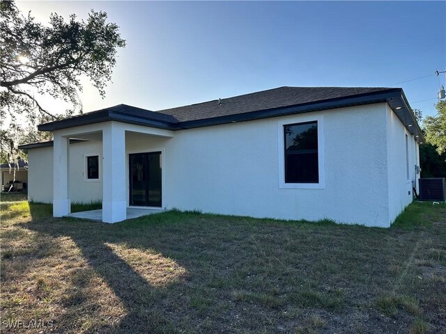 back of house featuring a lawn, stucco siding, cooling unit, and a shingled roof