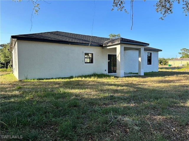 back of property featuring roof with shingles, stucco siding, and a yard
