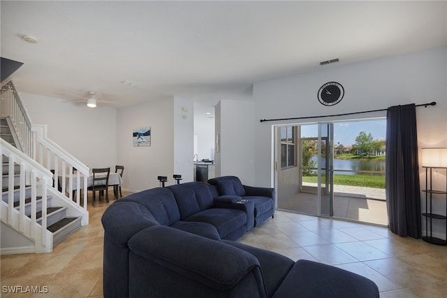 living area with ceiling fan, visible vents, light tile patterned floors, stairway, and a water view