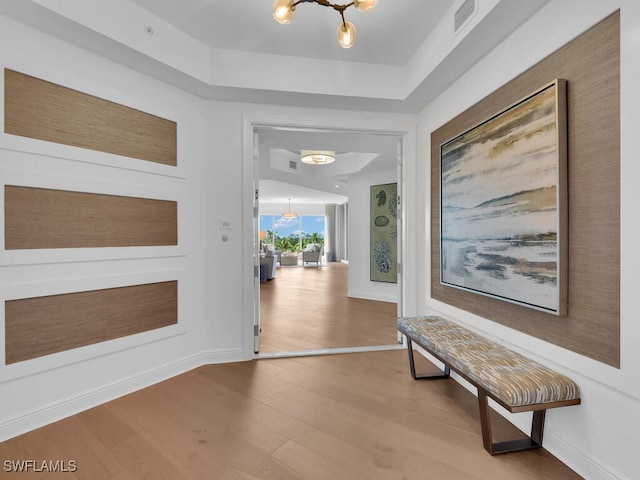 hallway featuring wood finished floors, baseboards, and a raised ceiling