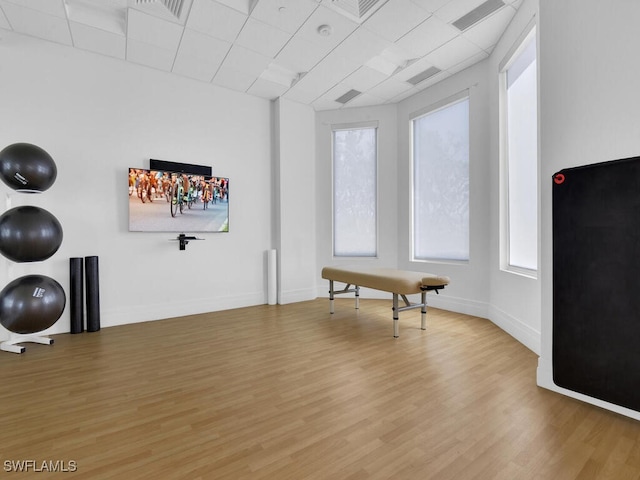 exercise room with a drop ceiling, light wood-style flooring, and baseboards