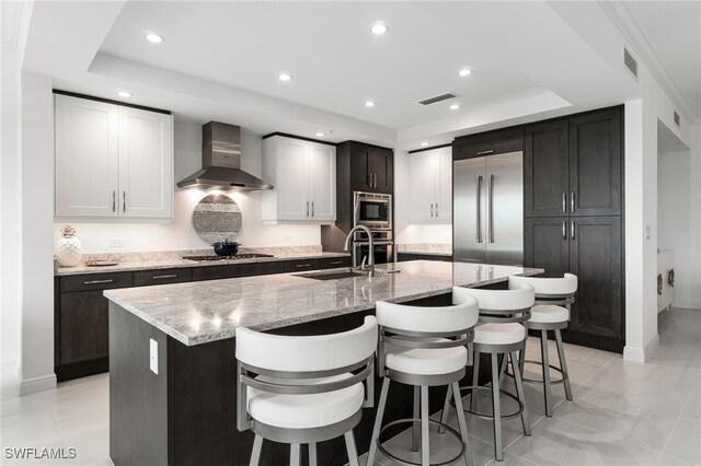 4800 Pelican Colony Blvd Unit 303, Bonita Springs, FL 34134 - kitchen with wall chimney exhaust hood, built in appliances, a tray ceiling, a breakfast bar area, and a kitchen island with sink