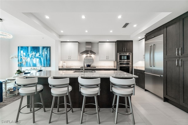 4800 Pelican Colony Blvd Unit 303, Bonita Springs, FL 34134 - kitchen with built in appliances, wall chimney range hood, light stone countertops, a center island with sink, and a breakfast bar