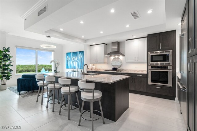 4800 Pelican Colony Blvd Unit 303, Bonita Springs, FL 34134 - kitchen featuring stainless steel appliances, a raised ceiling, wall chimney range hood, a kitchen island with sink, and a kitchen bar