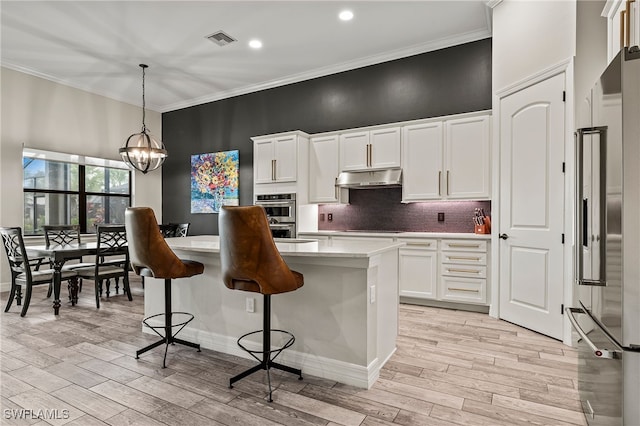 4424 Owens Way, Ave Maria, FL 34142 - kitchen with appliances with stainless steel finishes, white cabinetry, light wood-style flooring, ornamental molding, and a kitchen bar