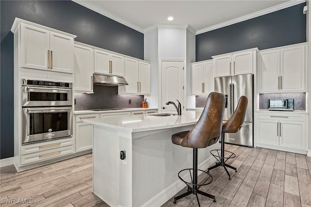 4424 Owens Way, Ave Maria, FL 34142 - kitchen featuring stainless steel appliances, under cabinet range hood, a sink, white cabinets, and ornamental molding