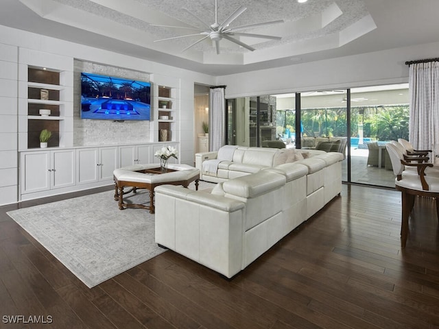 living area with a raised ceiling, built in features, ceiling fan, and dark wood finished floors