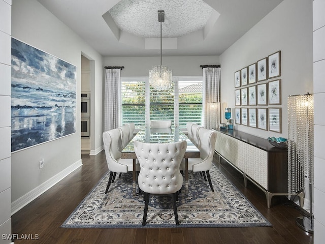 dining area with a tray ceiling, a chandelier, hardwood / wood-style floors, and baseboards