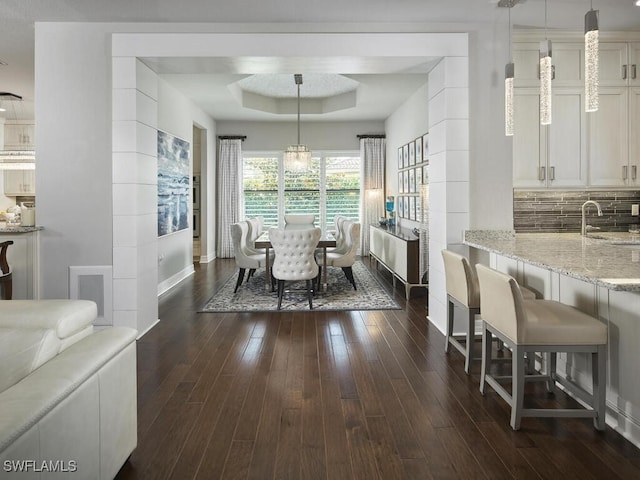 dining room featuring a tray ceiling, dark wood-style flooring, and baseboards