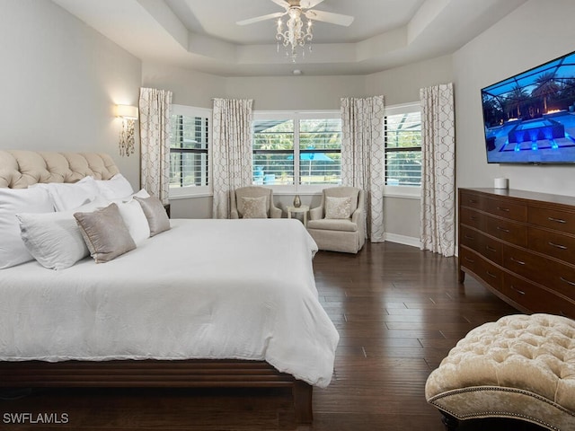bedroom featuring dark wood-style flooring, a tray ceiling, baseboards, and a ceiling fan