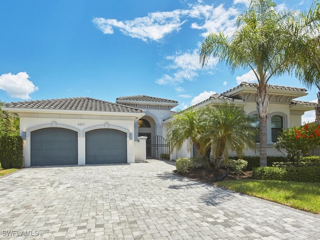 mediterranean / spanish home featuring a garage, decorative driveway, a tiled roof, and stucco siding