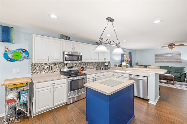 kitchen featuring a peninsula, light countertops, white cabinets, a sink, and appliances with stainless steel finishes