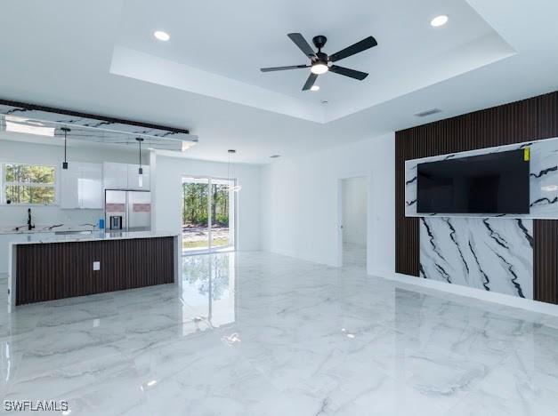 unfurnished living room featuring marble finish floor, ceiling fan, recessed lighting, and a raised ceiling