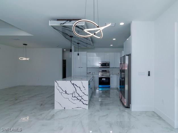 kitchen with white cabinets, appliances with stainless steel finishes, hanging light fixtures, a chandelier, and a center island