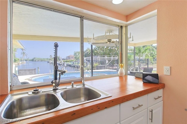 147 Coral Dr, Fort Myers, FL 33905 - kitchen featuring butcher block counters, a sink, a water view, white cabinetry, and a textured wall