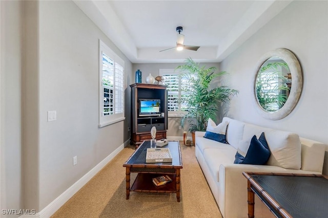 living area with baseboards, a ceiling fan, a tray ceiling, and light carpet