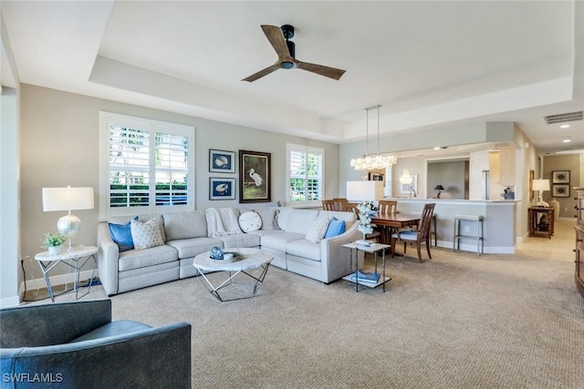carpeted living room featuring baseboards, visible vents, a raised ceiling, and ceiling fan with notable chandelier
