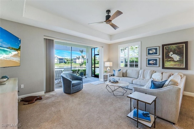 living area with carpet floors, a ceiling fan, a tray ceiling, and baseboards