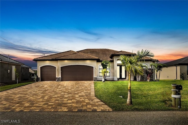 mediterranean / spanish house featuring a tile roof, a lawn, a garage, decorative driveway, and stucco siding