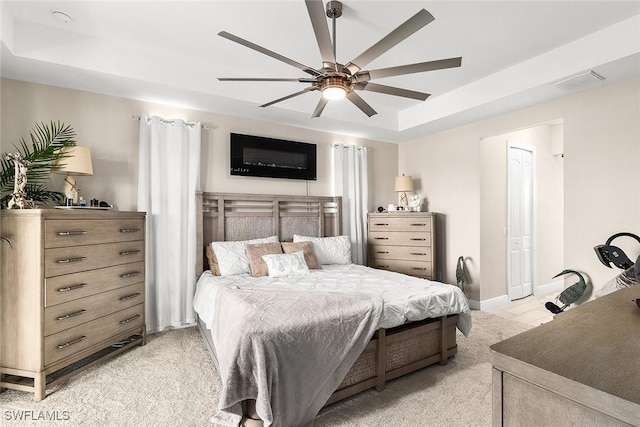 bedroom with a ceiling fan, a tray ceiling, light colored carpet, and visible vents