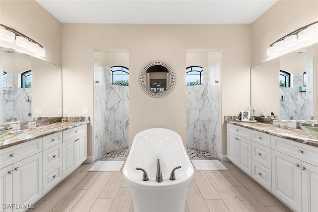full bath featuring a marble finish shower, a soaking tub, wood finish floors, and two vanities