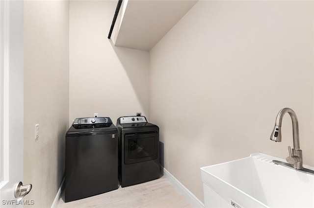 washroom with laundry area, light wood-style floors, baseboards, a sink, and independent washer and dryer