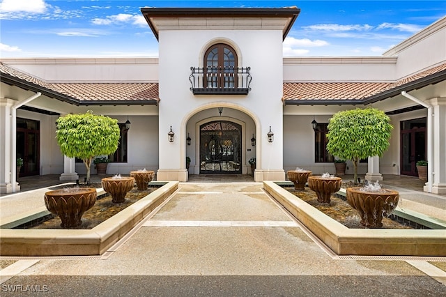 view of exterior entry with stucco siding, a tile roof, and a balcony
