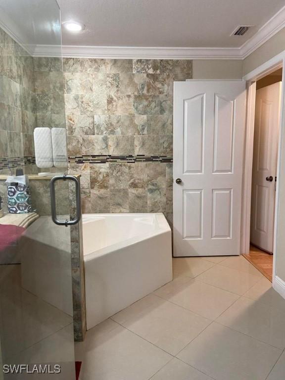bathroom with crown molding, tile patterned floors, a bath, tile walls, and a stall shower