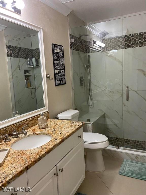 bathroom featuring toilet, a marble finish shower, vanity, and tile patterned floors