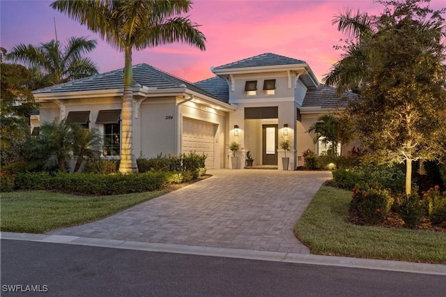 mediterranean / spanish-style home with a garage, a front yard, decorative driveway, stucco siding, and a tiled roof