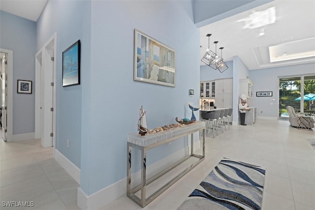 hall featuring baseboards, a tray ceiling, and light tile patterned flooring
