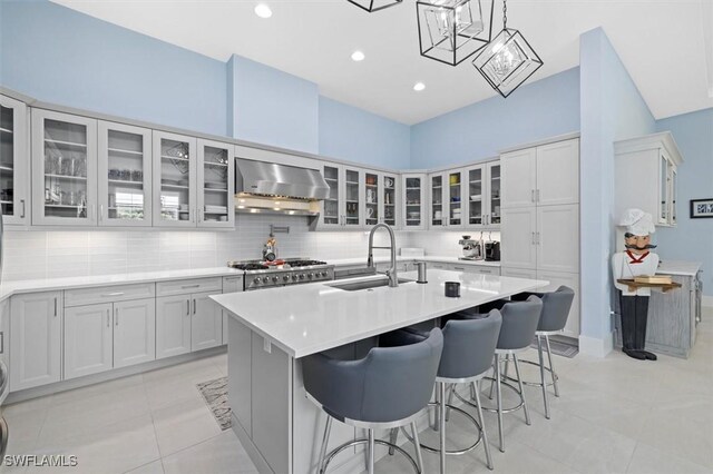 kitchen featuring a sink, decorative backsplash, exhaust hood, and a center island with sink
