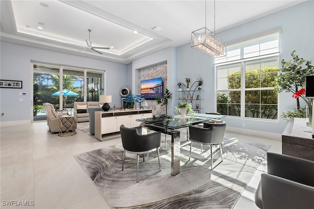 dining room with ceiling fan with notable chandelier and a tray ceiling