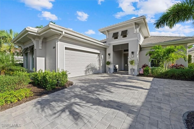 mediterranean / spanish-style home with a tiled roof, decorative driveway, an attached garage, and stucco siding