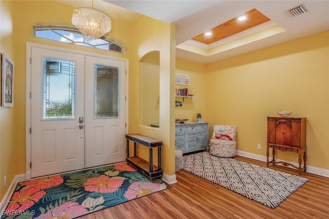 foyer entrance with wood finished floors, a tray ceiling, a notable chandelier, visible vents, and baseboards