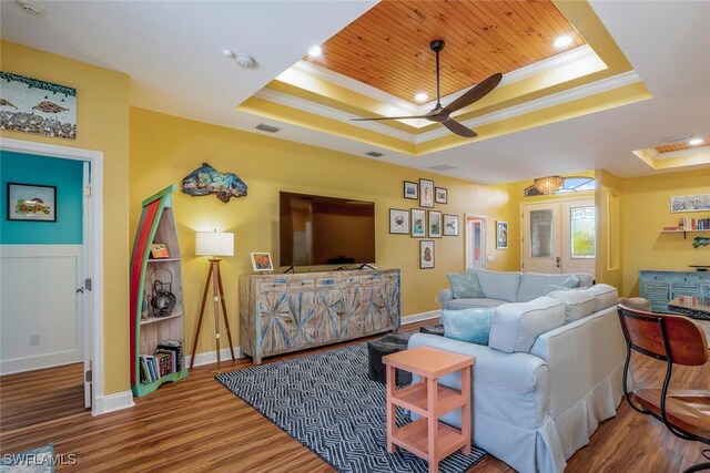 living room with a tray ceiling, crown molding, and wood finished floors