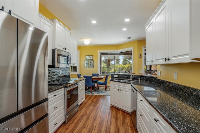 kitchen with recessed lighting, a sink, wood finished floors, stainless steel appliances, and white cabinets