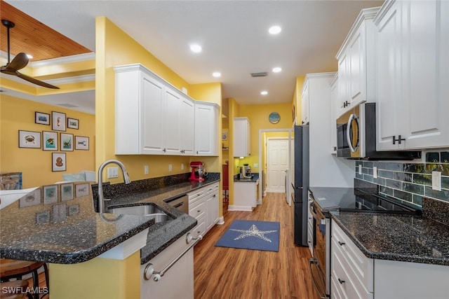kitchen featuring a peninsula, light wood finished floors, a breakfast bar, a sink, and appliances with stainless steel finishes