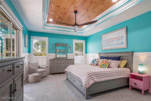 bedroom featuring a tray ceiling, wood ceiling, wainscoting, and light colored carpet