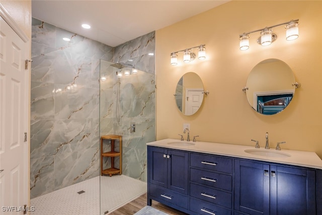 full bath with a marble finish shower, double vanity, a sink, and wood finished floors